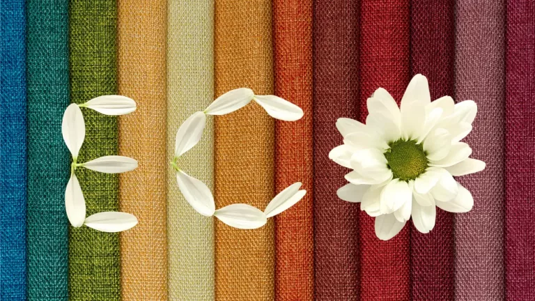 A variety of colored fabric swatches with a white petal recycling symbol and a white daisy flower on top, possibly symbolizing the harmony between nature and sustainable textiles.