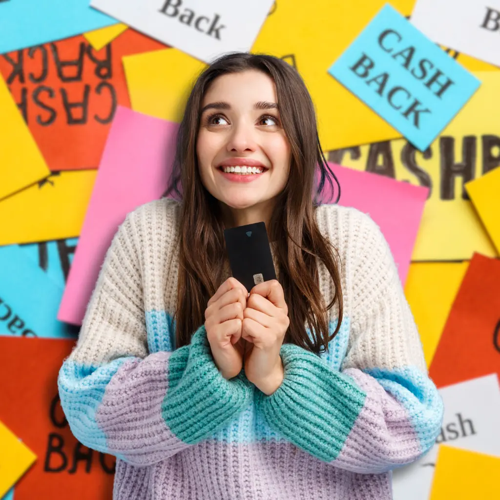 Cashback and Reward Programmes - a young woman looking upwards with an excited and hopeful expression. She is holding a credit card with both hands close to her chest.