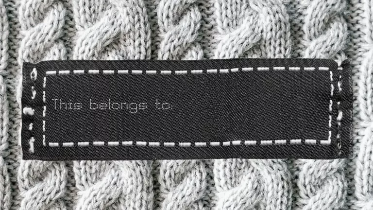 A clothing label on a knitted fabric with the text "This belongs to:" indicating a space for a name to be added for identification.