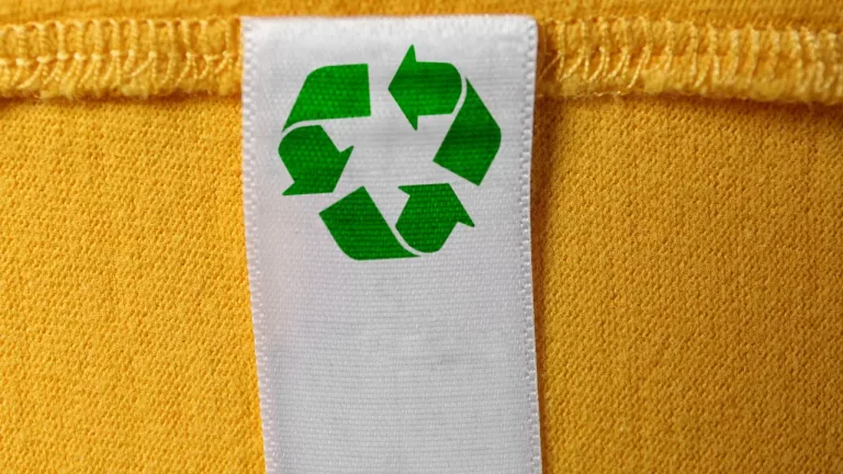 a close-up of a white fabric label with a green recycling symbol, sewn onto a yellow textile background.