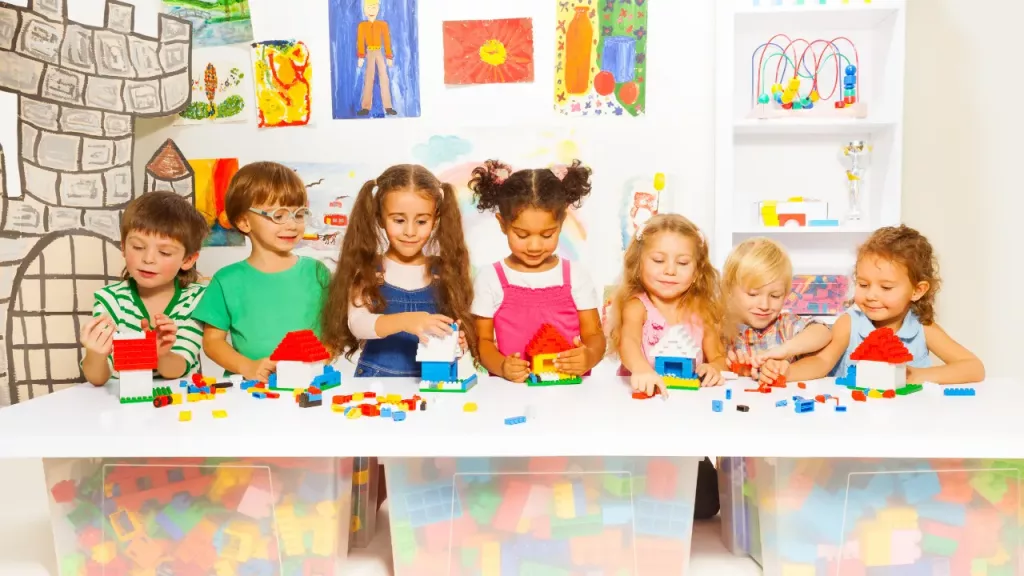 six children of various ethnicities engaged in play with colorful building blocks at a white table.