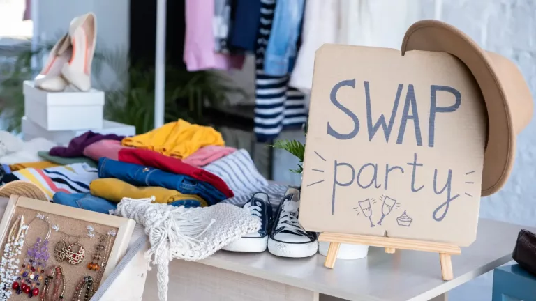 a display of various clothing items and accessories arranged on a table for a "Swap Party," as indicated by a handmade sign with the words "SWAP party" prominently displayed.