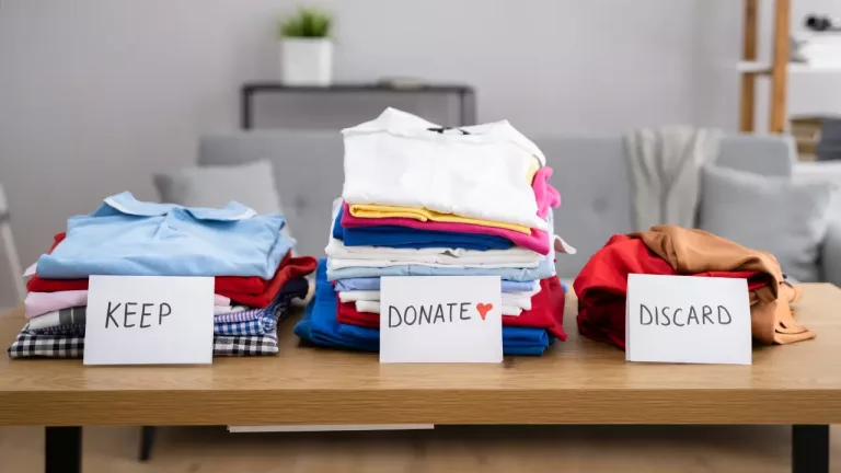 three labeled piles of clothes on a table: "KEEP," "DONATE," and "DISCARD," indicating a sorting process for clothing organisation.
